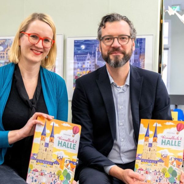 Bildbeschreibung: Christine Faust sitzt links und Steffen Schier sitzt rechts und halten das neue Wimmelbuch in den Händen. Beide lächeln in die Kamera.