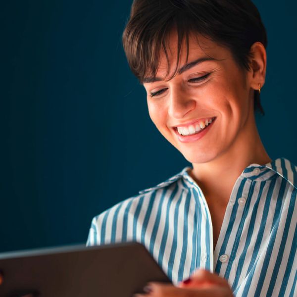 Bildbeschreibung: Frau hält Tablet in der Hand und lächelt.